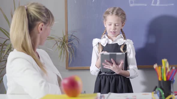Portrait of Charming Caucasian Girl in School Uniform Declaiming To Middle Aged Teacher Sitting alt