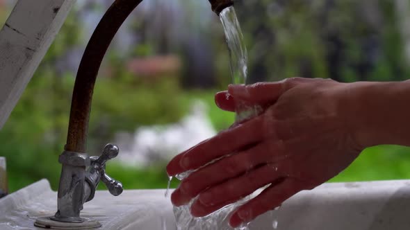a Woman Carefully Washes Her Hands Under an Old Faucet on the Street. Close Up alt