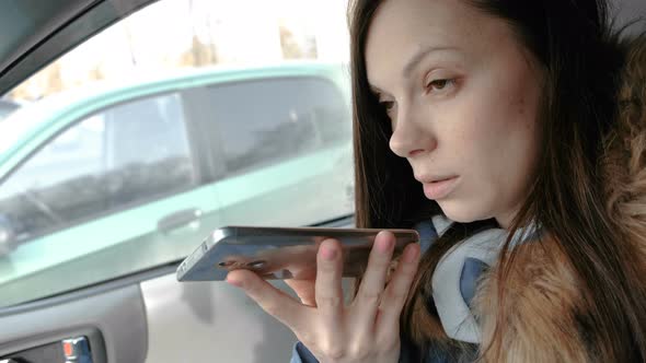 Young Beautiful Woman Speak a Voice Message on a Mobile Phone Sitting in the Car