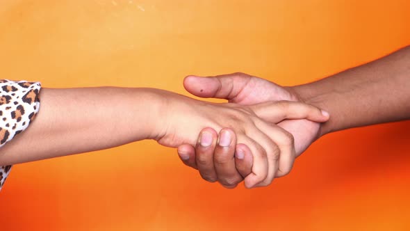 Close Up of Couple Holding Hands Against Orange Background. alt