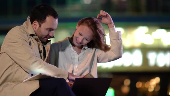 Young Co-workers Woman and Man Sitting Outside Working on Laptop Computer. alt