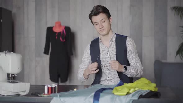 Portrait of Confused Caucasian Man Putting on Eyeglasses and Sighing As Sitting at the Table in alt