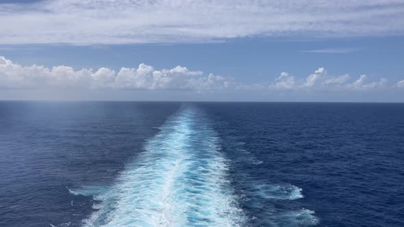 Wake behind large ship on the ocean with sunny blue sky and clouds on horizon alt
