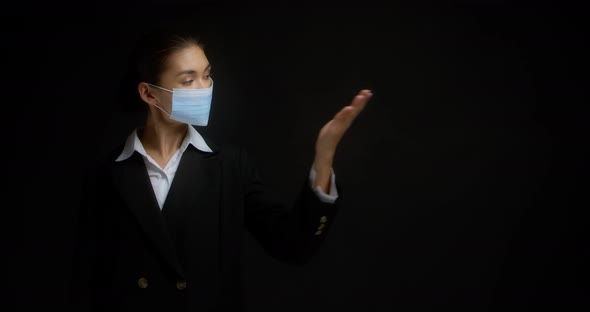 Woman in a Medical Mask Points with Her Palm to an Empty Copy Space on the Right