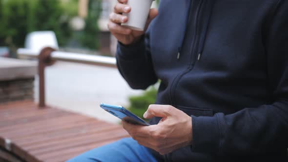 Closeup of Hands of a Man with Coffee in a Paper Cup and a Smartphone