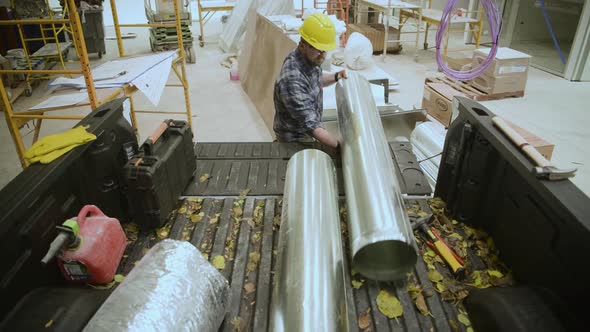 Warehouse Construction Site. Caucasian HVAC Construction Worker Unloading Pieces of Air Duct alt
