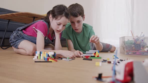 Girl and a boy playing and constructing with toy bricks on the living room floor alt
