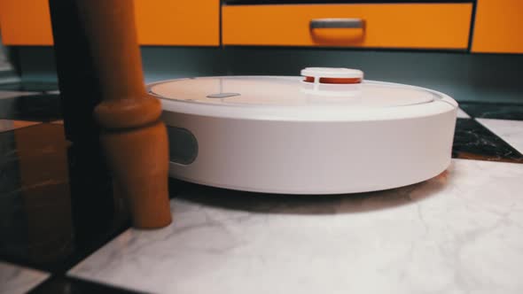 The Robot Vacuum Cleaner Cleans in the Modern House on the Tiles Floor at Kitchen alt