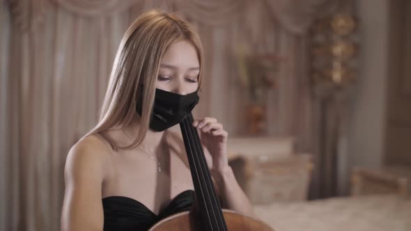 beautiful girl in mask playing the cello in a beautiful room. repetition . close-up. Pandemic. Covid