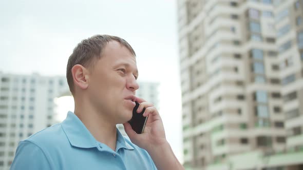 Portrait of a Man Talking on a Mobile Phone Against the Background of Skyscrapers alt