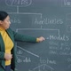 Portrait of Female English Teacher Pointing at Blackboard and Explaining During Distant Class - VideoHive Item for Sale