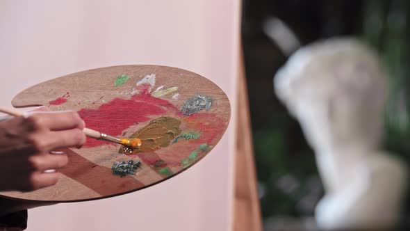 A Young Woman in Art Workshop Mixing an Orange and Blue Colors on the Palette alt