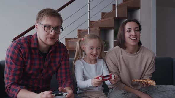 Woman, Man and They Child Playing in Video Games and Eating Pizza alt