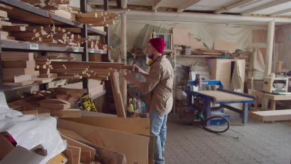 Carpenter Taking Wooden Plank for Work and Putting Safety Earmuffs alt