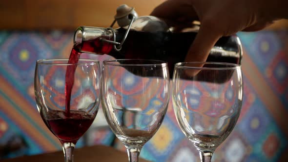 Pouring house wine in glasses. Filling three glasses with red young wine