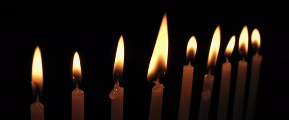 Lit Hanukkah candles burning in a dark room, slow motion alt