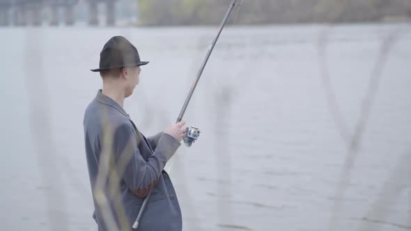 Young Fisherman in a Jacket and a Cap with a Brim in the Early Morning Catch Fish alt