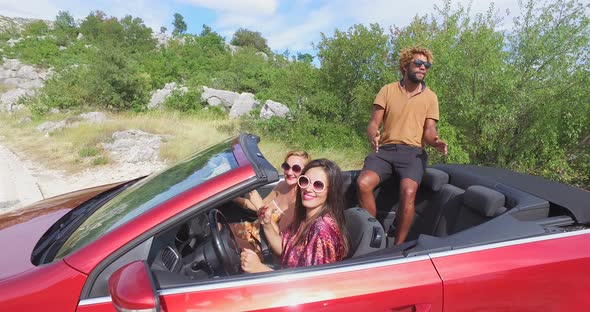 Handsome black man sitting on hood of convertible dancing with friends, graded alt