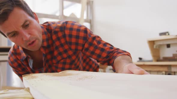 Caucasian male surfboard maker checking a surfboard after polishing alt