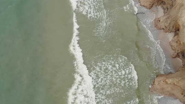 Aerial View of Ocean Waves Crashing Against the Steep Coastline on a Wooded Coast alt