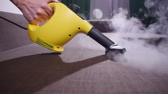Furniture and Apartment Cleaning Concept. Man Cleaning Couch with Steam Cleaner at Home alt