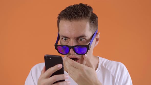 Scared and Shocked Man Takes Off Sunlasses Reacting Message on Smartphone