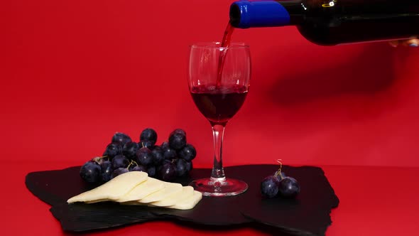 Pouring Red Wine Into A Glass. Rose Wine With Cheese And Grapes. Red Wine On Luxury Red Background