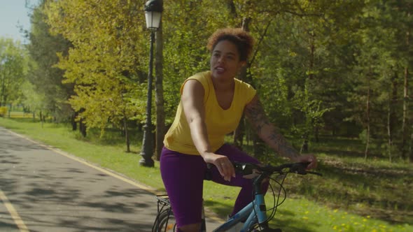 Cheerful Pretty African Female Cyclist Riding on Bike Through Park alt