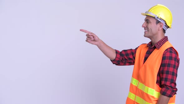 Profile View of Young Happy Hispanic Man Construction Worker Pointing Finger