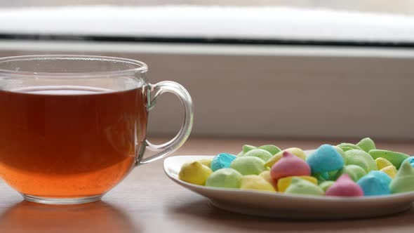 A Large Mug of Tea and Colorful Sweets in a Plate on the Windowsill By the Window in Winter