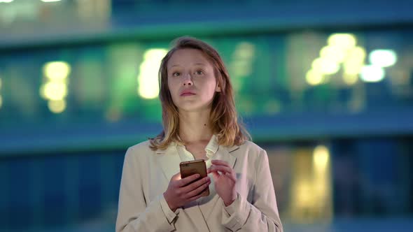Blonde Woman with Smartphone Near Business Building Waiting and Deciding To Make a Call. alt