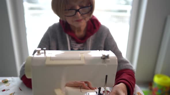 Pensioner Woman Wearing Glasses Sews Home Textiles on a Sewing Machine alt