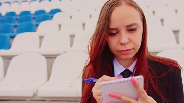 Young Woman with Notepad Pen Sitting on Stadium Bleachers Alone alt