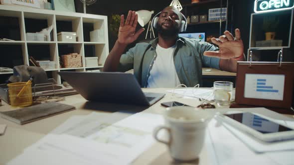 Relaxed Afro Manager Chilling in Headphones Near Laptop at Modern Workplace alt