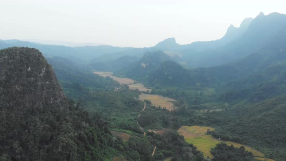 Aerial: flying over rice paddies unique valley scenic cliffs rock pinnacles tropical jungle Laos alt