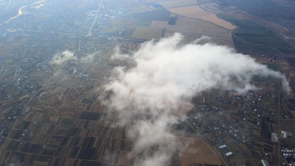 Aerial View From High Altitude of Distant City Covered with Puffy Cumulus Clouds Flying By Before alt