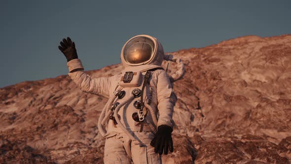 Astronaut Stands on a Rock Waving His Hand Against the Sky alt