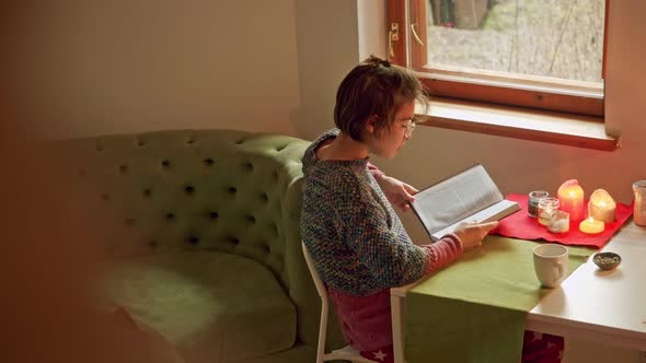 a Woman in a Cozy House at a Table Reads a Book Waiting for the Pandemic of Coronavirus and Keeping alt