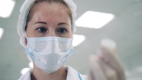 Female Doctor in a Face Mask is Looking at a Medicine Tub alt