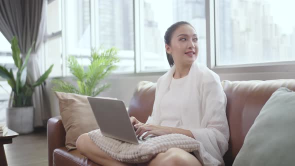 Asian girl looks out the window while working at home on laptop. alt