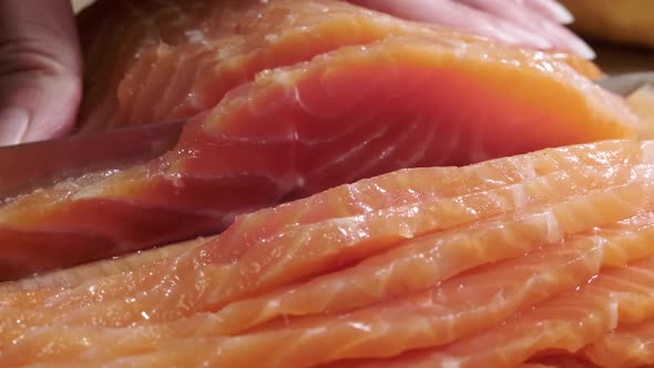 A woman's hand cuts fresh salmon by slices. 