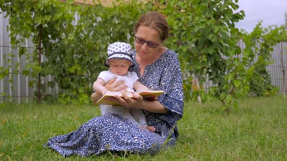 Ladies Reading Book. Grandmother with Granddaughter Sitiing on Green Grass. Baby Girl with Nanny