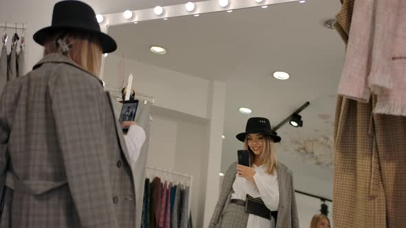 Stylish Young Woman Taking Selfie in Fitting Room Against Big Mirror of Modern Boutique alt