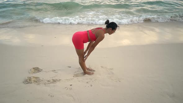 Young Woman in a Sport Suit Practicing Yoga on the Beach at Sunrise Near the Sea