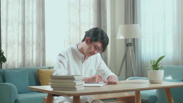 Asian Man Student Writing In The Notebook On The Table While Studying At Home alt