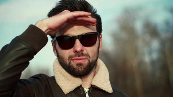 Businessman In Bomber Standing Near River And Thinking. Man Stands On Beach And Looking At Distance. alt