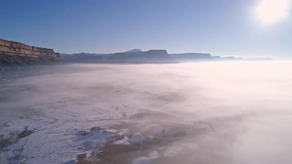 Panning aerial view of thin layer of fog over snow in the desert alt