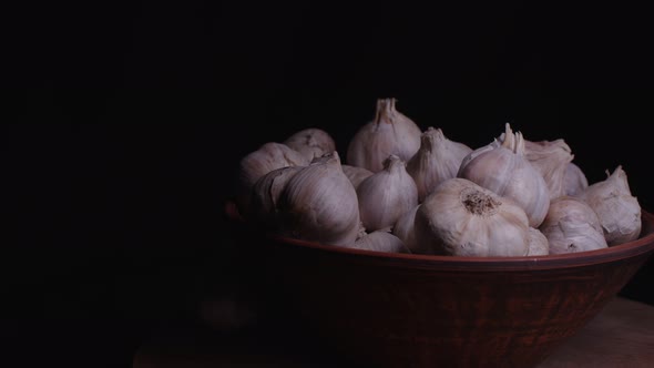 Pile of whole bulbs of garlic in ceramic bowl on table. alt