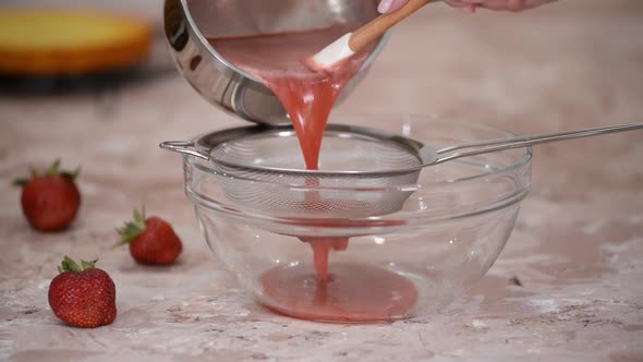 Professional cook hands prepares strawberry berry puree by rubbing through a sieve.