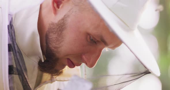Closeup Face of Young Male Bearded Beekeeper in White Protective Suit Smiling Looking Down Apiary in alt